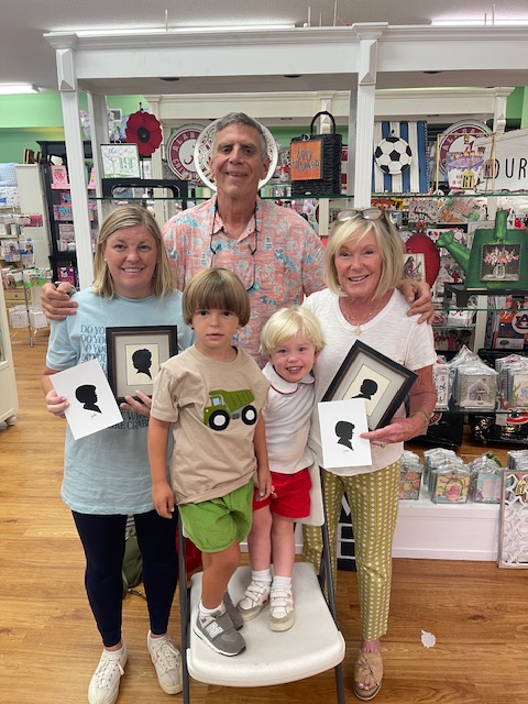 clay rice posing with a family of four holding commisioned sillhouette portraits